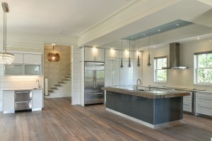 Custom kitchen with large island with sink. Stairwell, wood floor and white bar area. 